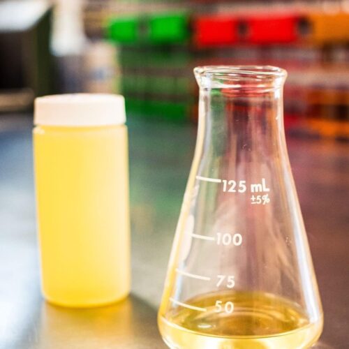 Yellow oil or fuel in a test kit bottle beside a beaker of oil