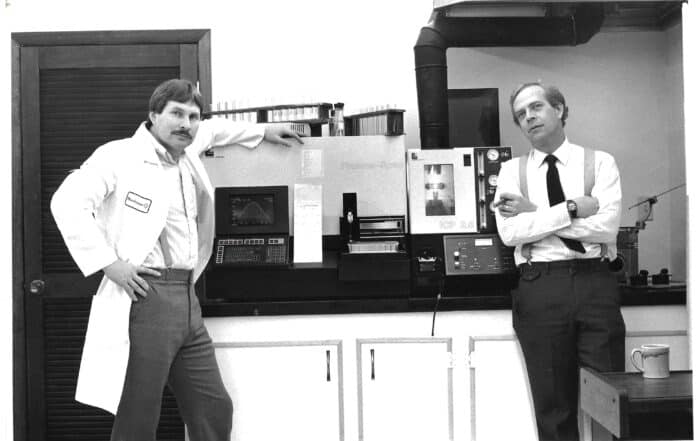 Black and white photo of Jim and Bob in 1985, standing by their brand-new, state-of-the-art ICP spectrometer.