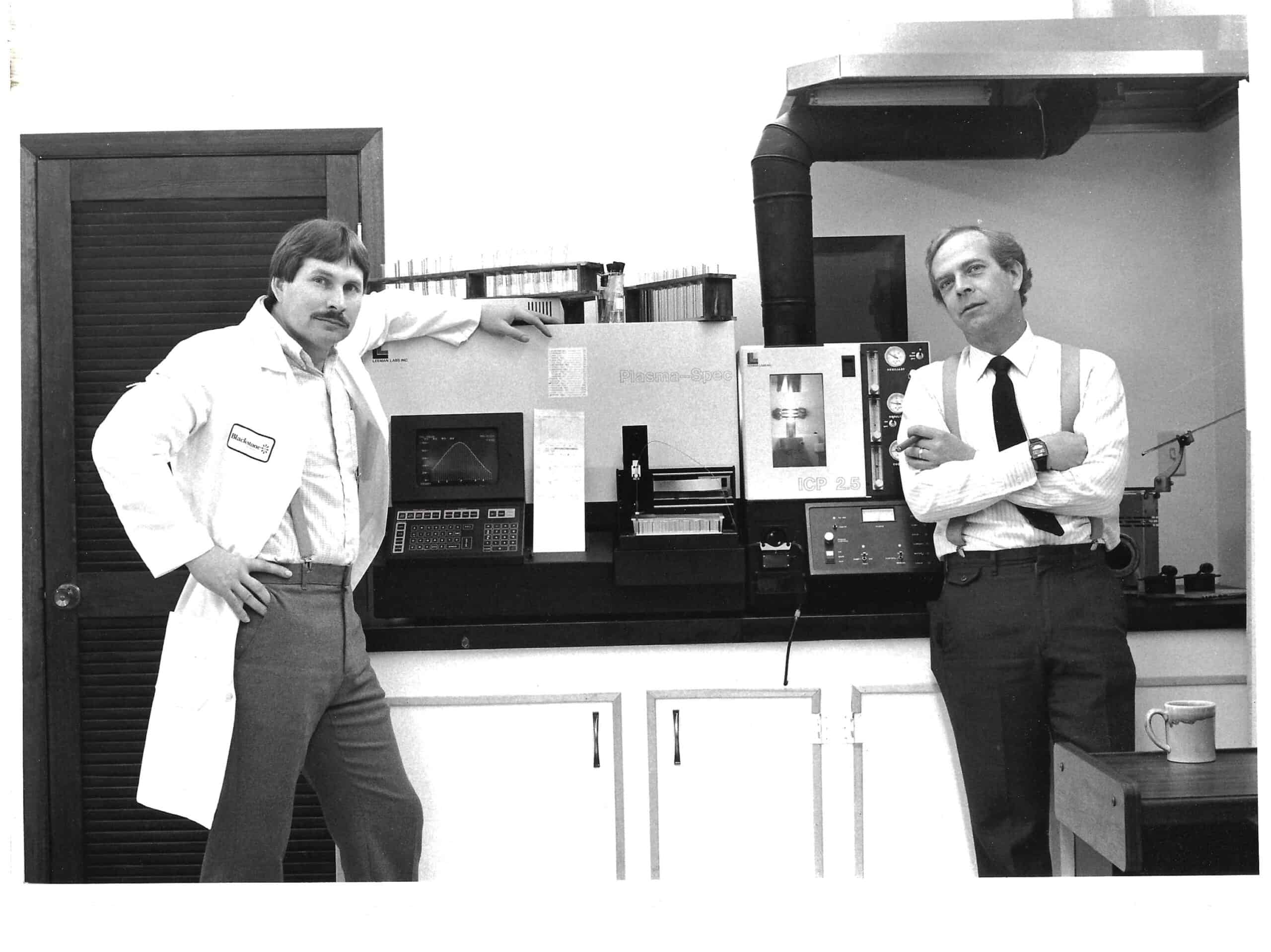 Black and white photo of Jim and Bob in 1985, standing by their brand-new, state-of-the-art ICP spectrometer.