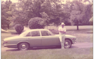 Jim Stark wearing a dapper hat and standing next to his baby blue Jaguar