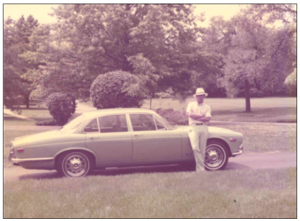 Jim Stark wearing a dapper hat and standing next to his baby blue Jaguar